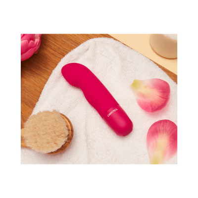 Vibrador cor-de-rosa numa toalha branca com escova de madeira e pétalas cor-de-rosa