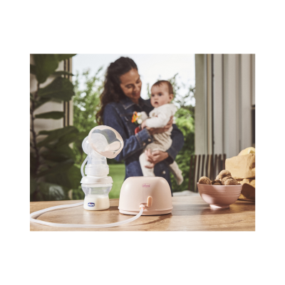 Extractor de leite materno com garrafa sobre mesa de madeira e mulher segurando bebé