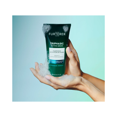 Mãos segurando tubo verde escuro de shampoo René Furterer com espuma