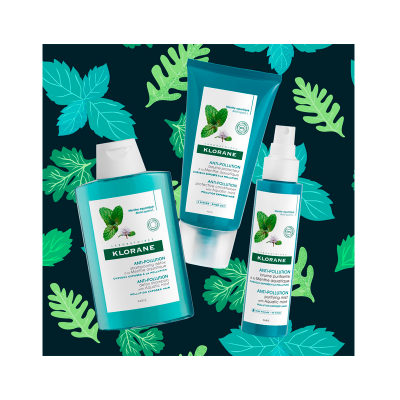Produtos Klorane Anti-Pollution com Menta sobre fundo de folhas verdes