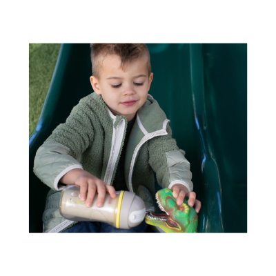 Criança em casaco verde a brincar com mamadeira e brinquedo dinossauro