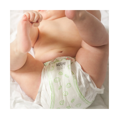 Bebé com fralda MUUMI BABY branca com padrão verde deitado numa cama branca