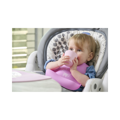 Bebé sentado numa cadeira alta a usar babete rosa e a beber de um copo rosa