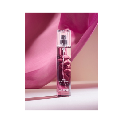 Frasco de perfume rosa transparente sobre superfície branca com pano rosa ao fundo