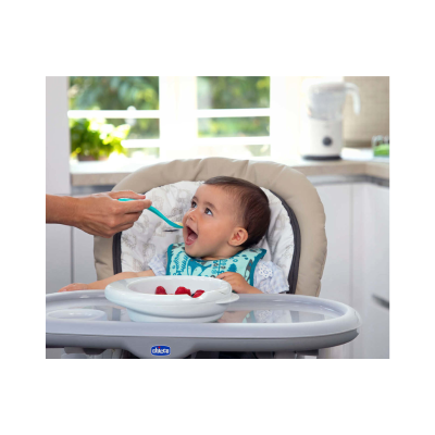 Bebé numa cadeira alta Chicco a ser alimentado com colher azul na cozinha
