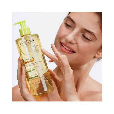 Frasco A-Derma Exomega Control óleo de banho 500 ml com tampa de bomba verde claro atrás de mulher sorridente