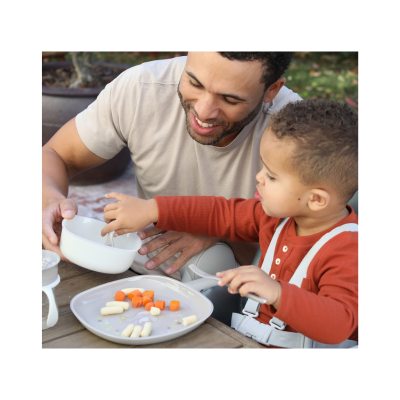 Pratos e tigelas brancas com vegetais em mesa de madeira com criança e adulto ao ar livre