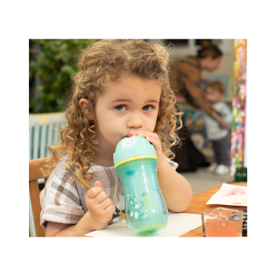 Menina bebendo de copo plástico verde com tampa azul clara e desenho de raposa