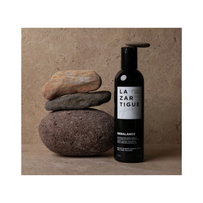 Frasco preto de champô com rótulo branco junto a pedras empilhadas numa superfície bege