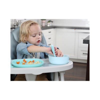 Criança a comer em cadeira de refeição com pratos azuis e comida numa cozinha