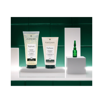 Produtos de cuidado capilar RENE FURTERER Triphasic em tubos e ampola sobre suportes brancos com fundo verde