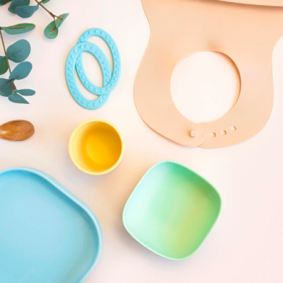 Utensílios para bebé em cores pastel com babete de silicone bege, tigelas, copo e colher, decoração com folhas verdes