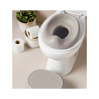 Sanita branca com assento elevatório cinzento claro e degrau cinzento junto a papel higiénico e planta