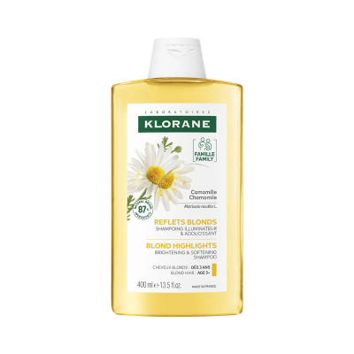 Frasco amarelo de champô Klorane com tampa branca e rótulo branco com texto e imagem de camomila