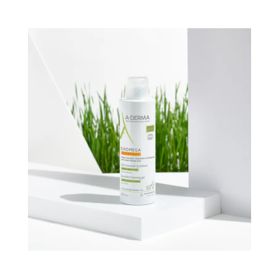 Frasco de gel espumante emoliente A-DERMA EXOMEGA CONTROL colocada numa plataforma branca com plantas verdes ao fundo