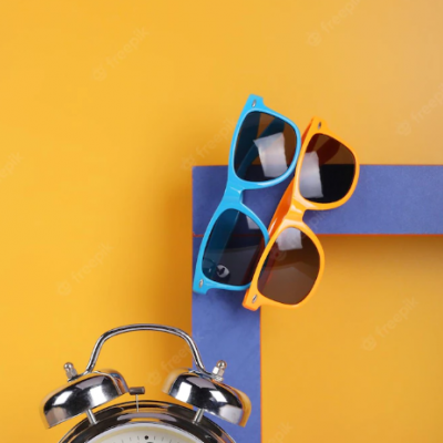 Dois óculos de sol coloridos sobre superfície azul e fundo amarelo com despertador cromado