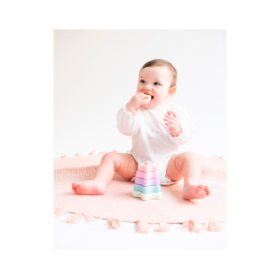 Bebé com body branco a brincar com brinquedo de empilhar em tapete rosa