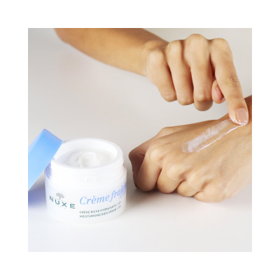 Creme hidratante NUXE com tampa azul sendo aplicado na mão.
