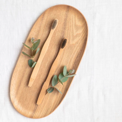 Duas escovas de dentes de madeira numa placa oval de madeira com ramos verdes