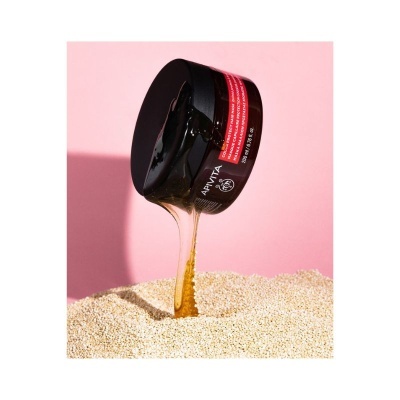 Frasco preto a escorrer líquido dourado viscoso sobre sementes claras com fundo rosa