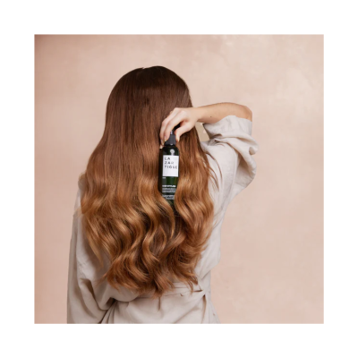 Mulher com cabelo longo e ondulado segurando frasco de produto de cabelo LAZARTIGUE