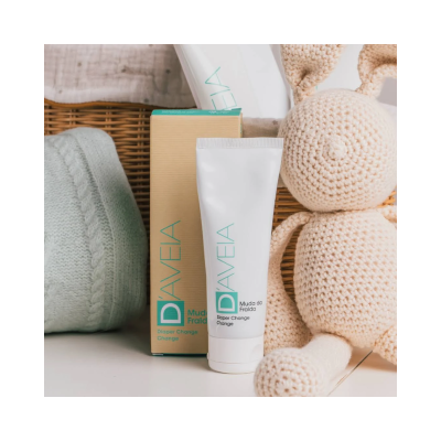 Tubo branco e embalagem castanha com creme DAVEIA junto a almofada cinza e brinquedo de crochê bege