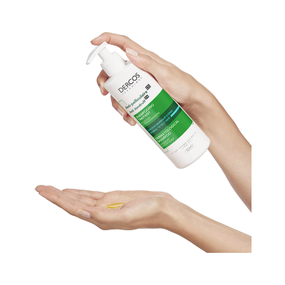 Embalagem branca com dispensador, rótulo verde e branco DERCOS VICHY, líquido amarelo na mão