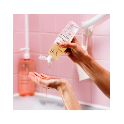 Mãos a verter gel amarelo de garrafa transparente com rótulo em casa de banho cor-de-rosa