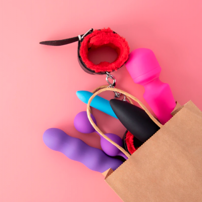 Brinquedos sexuais de silicone coloridos e algema vermelha e preta saindo de saco de papel castanho