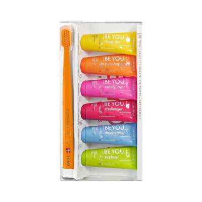 Conjunto de pastas de dentes coloridas e escova de dentes laranja num suporte branco