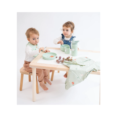 Mesa infantil com acessórios verdes claros e duas crianças sentadas