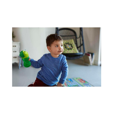 Copo infantil verde com tampa e bico segurado por criança dentro de casa