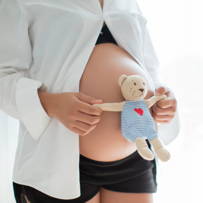 Pessoa grávida segurando urso de pelúcia listrado azul e branco com coração vermelho