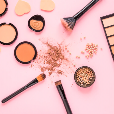 Produtos de maquilhagem em fundo rosa com pincéis, pós compactos, pérolas e paleta de sombras