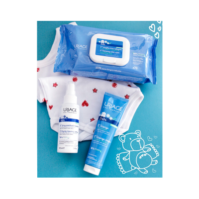 Produtos de cuidado para bebé Uriage sobre fundo azul com roupa branca de bebé e ilustração de ursinho.