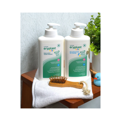 Duas embalagens de produtos para bebé, escova de cabelo, toalha branca e planta verde sobre superfície de madeira