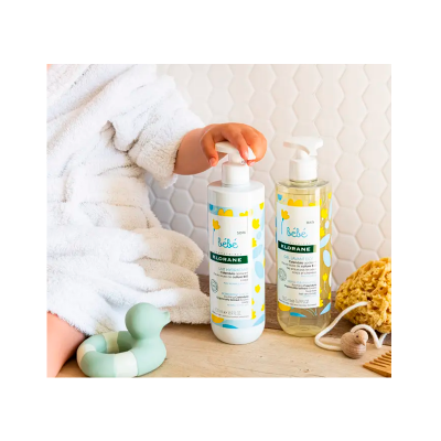 Dois produtos de cuidado para bebé da Klorane sobre uma superfície de madeira com brinquedo e esponja ao lado