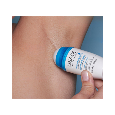 Desodorizante roll-on Uriage branco e azul aplicado na axila com fundo azul.
