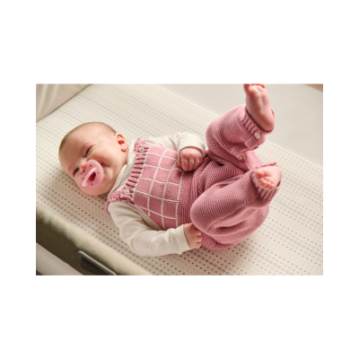 Bebé deitado com body branco e jardineira rosa de malha com padrão xadrez
