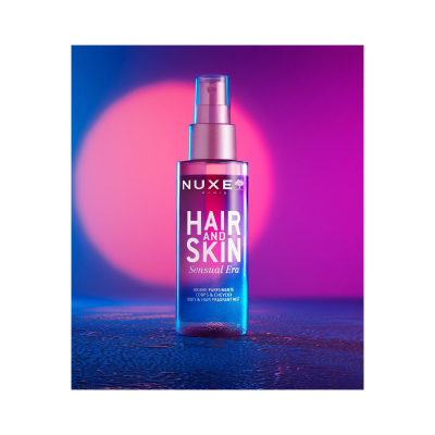 Frasco de spray NUXE HAIR AND SKIN Sensual Era em fundo azul e rosa