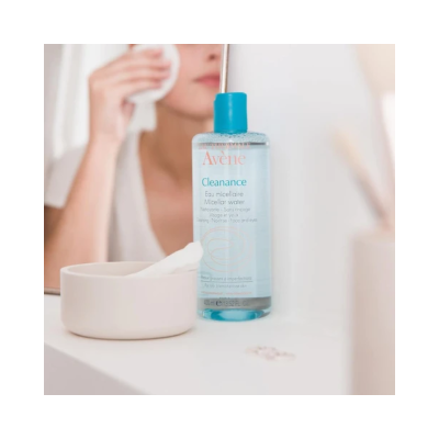 Garrafa de limpeza micelar Avène Cleanance com recipiente branco e pessoa a limpar o rosto ao fundo