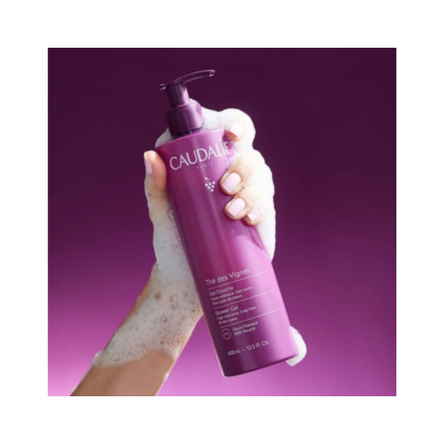 Mão com espuma segurando frasco roxo de gel de banho Caudalie