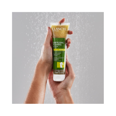 Tubo de esfoliante ELANCYL Energizing Foaming Scrub segurado por duas mãos com fundo cinza e gotas de água caindo