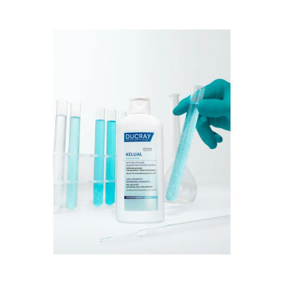 Frasco branco de champô Ducray Kelual Squalorn com tubos de ensaio e mão com luva azul