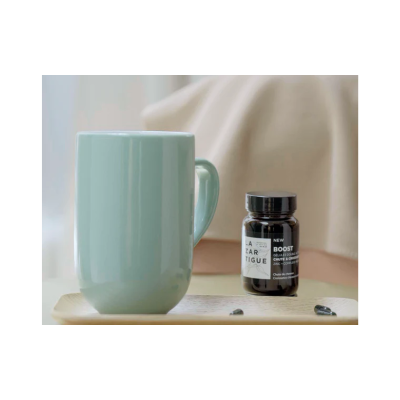 Frasco de suplemento preto com cápsulas e caneca azul clara numa base clara