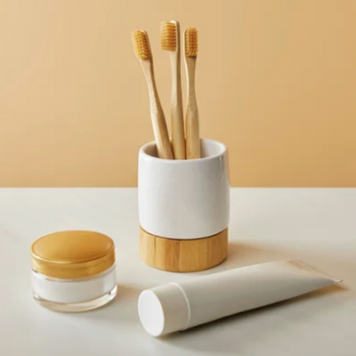 Três escovas de dentes de madeira num suporte branco e madeira com tubo branco e frasco transparente com tampa dourada