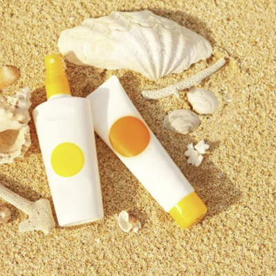 Dois frascos de protetor solar branco e amarelo sobre areia com conchas e corais