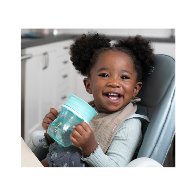 Criança sorridente num cadeirão alto a segurar um copo azul numa cozinha