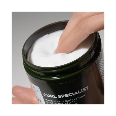 Frasco verde com creme branco e dedo dentro do creme