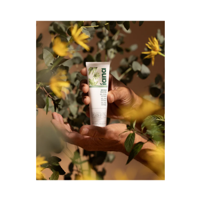 Tubo branco de gel frio liana segurado entre mãos com plantas e flores amarelas ao fundo